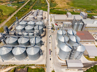 Grain storage facility located near a rural area with many silos and trucks on the road in the daytime © DSMT
