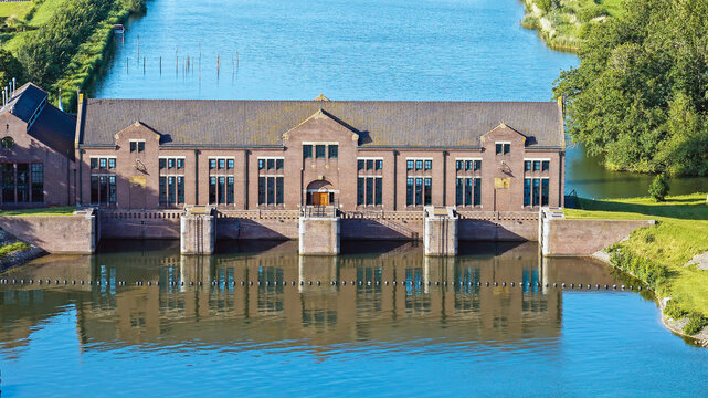 Aerial view of the Wouda pumping station, a historic brick building with large windows situated along a canal with calm water reflecting the structure, in Lemmer, Friesland, Netherlands.