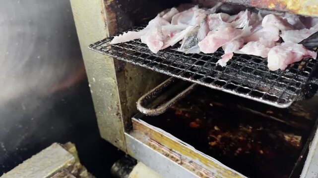 Grilling fresh Japanese sea bass offcuts on a wire mesh grill, Japan