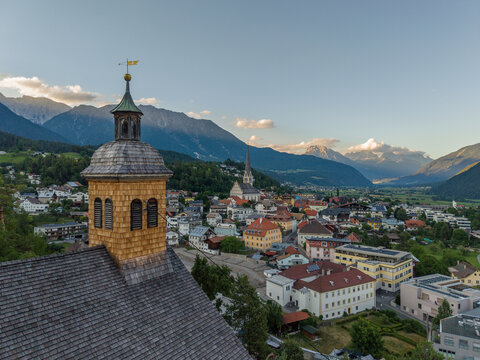 Aerial view of St. Laurentius Church with its wooden shingled tower overlooking the historic town of Imst nestled in the Austrian Alps during golden hour in Imst, Tyrol, Austria.
