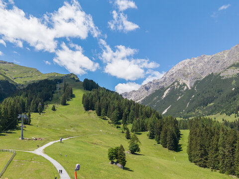 Aerial view of the alpine landscape in Imst featuring green mountain slopes, a cable car line, and a winding path under a bright blue sky in Imst, Tyrol, Austria.