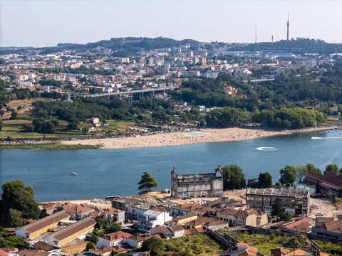 Aerial view of Praia Fluvial do Areinho along the Douro River with urban buildings, lush greenery, and a bridge in the background in Vila Nova de Gaia, Porto, Portugal.