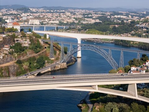 Aerial view of Ponte Infante Dom Henrique bridge spanning the Douro River, with historic and modern structures, green hills, and urban development in Vila Nova de Gaia, Porto, Portugal.