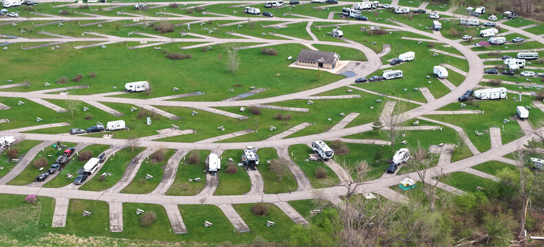 Aerial view of a spacious campground featuring numerous recreational vehicles parked on paved pads surrounded by lush green grass and trees in Monroe, Michigan, United States.