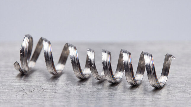 A close-up of a metallic spiral spring on a smooth surface. The spring is coiled and reflects light, showcasing its shiny texture and design.