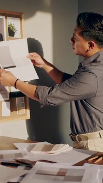 Vertical video: Reaching man in rolled sleeves matching print to cork board swatches, copy space
