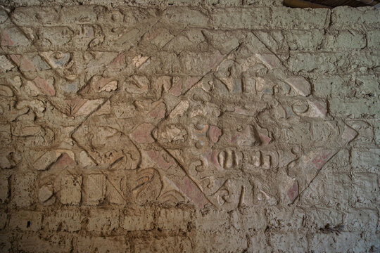 Close up of a heavily eroded adobe relief featuring the faded stylized face of the Moche deity Aiapaec at El Brujo, Peru