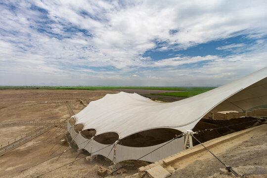 Aerial view of the Huaca Cao Viejo archaeological site with its large white tensile canopy covering the ruins, surrounded by green agricultural fields and desert landscape in El Brujo, Peru