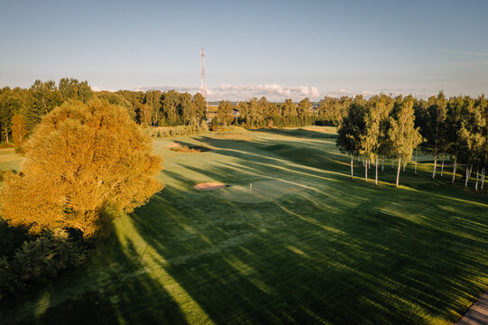Aerial view of a lush green golf course with sand bunkers and long tree shadows during golden hour in Valmiera, Valmiera, Latvija.