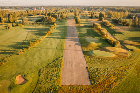Aerial view of a golf course with green fairways, sand bunkers, and long tree shadows during golden hour in Valmiera, Valmiera, Latvija.