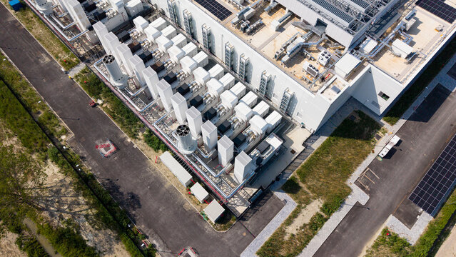 Aerial view of a modern hyperscale data center featuring rows of industrial cooling units, solar panels, and paved access roads in Melegnano, Lombardy, Italy.