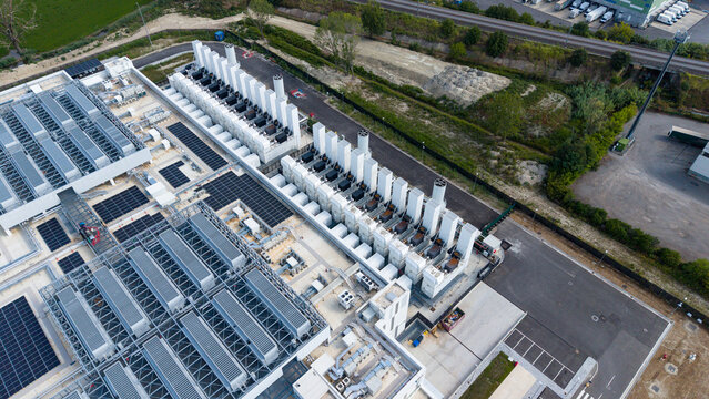 Aerial view of a modern hyperscale data center featuring rows of industrial cooling units and server infrastructure in Melegnano, Lombardy, Italy.