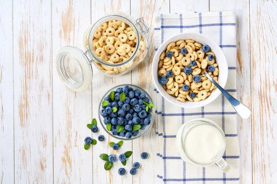 Healthy breakfast with corn hoops and blueberry on a white wooden table, top view.