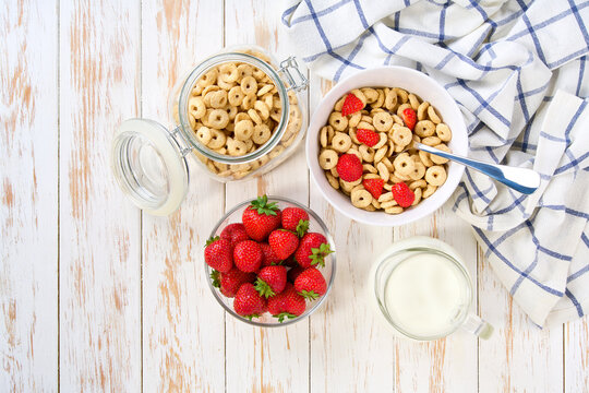 Quick breakfast for kids with corn hoops and strawberry on a light kitchen table, top view. Healthy corn flakes with milk for Breakfast with fruit.