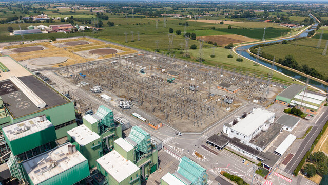 Aerial view of the Tavazzano power station featuring a large electrical substation, industrial buildings, and surrounding green fields with a canal in Tavazzano con Villavesco, Lombardy, Italy.