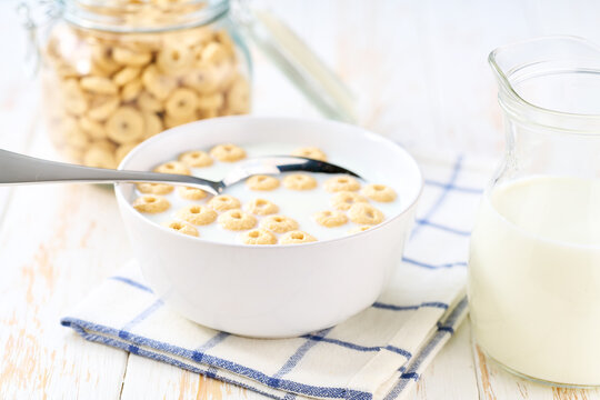 Making a healthy breakfast cereal using corn rings and milk on a white table.