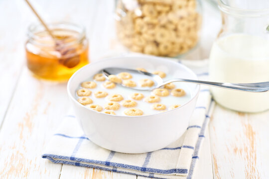 corn rings in a bowl with milk and honey on a white wooden table. Crispy cereal loops.