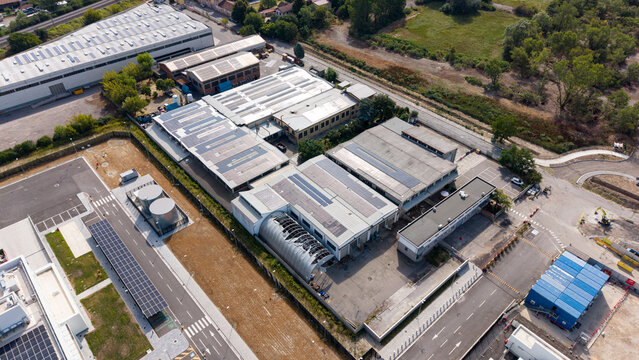 Aerial view of an industrial manufacturing and warehouse complex featuring extensive rooftop solar panels, highlighting sustainable energy integration in Melegnano, Lombardy, Italy.