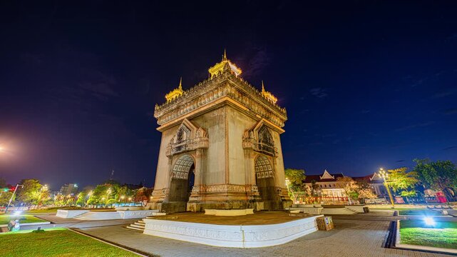 Time lapse The illuminated Patuxai Victory Arch stands proudly in Vientiane, Laos, framed by gardens and city lights. Captured during twilight, the scene highlights cultural heritage, national pride