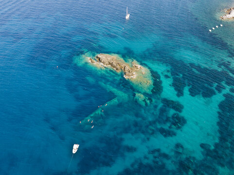 Aerial view of the Elviscot shipwreck submerged in clear turquoise waters near the rocky coast with swimmers and a small boat nearby in Pomonte, Province of Livorno, Italy.
