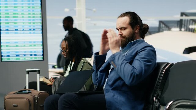 A businessman rubs his temples while dealing with a headache in an airport lounge, showing stress, fatigue and workload pressure near the gate before departure on a demanding work trip.