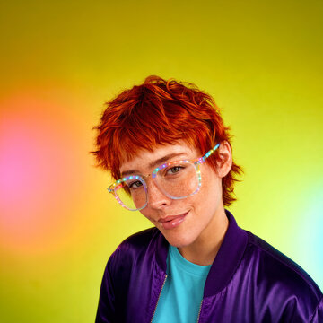 Confident young redhead with freckles wearing colorful illuminated glasses against a vibrant gradient background with copy space, futuristic fashion and joyful self expression