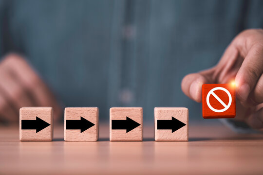Business stop concept with a hand placing a prohibition symbol block to prevent progress, represent halted operations, business interruption, workflow disruption, risk management, and decision making.