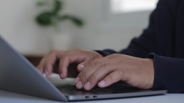 Close-up hand of a young man typing on a laptop keyboard computer at home office desk, freelance remote working online. Business technology concept.