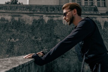 Side profile portrait of a stylish young man leaning on a concrete railing in a modern architectural environment. © Valeria Vaskovats