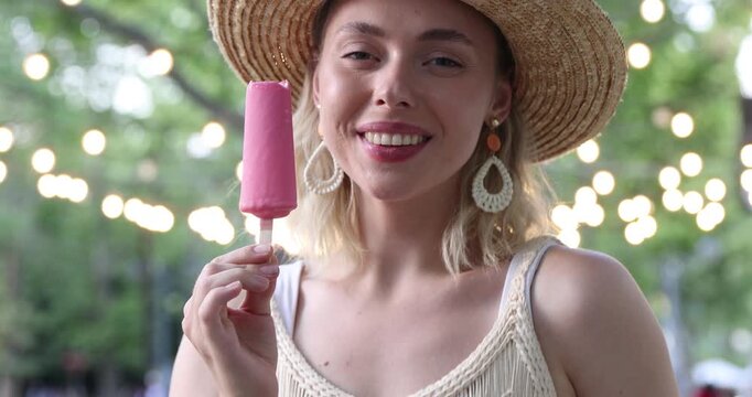 Happy woman in hat eating delicious ice pop in park
