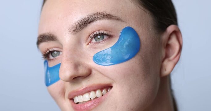 Beautiful woman with eye patches on light blue background, closeup