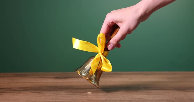 Woman ringing school bell at wooden table near chalkboard, closeup