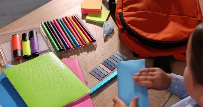 Little girl packing backpack for school at table indoors, closeup