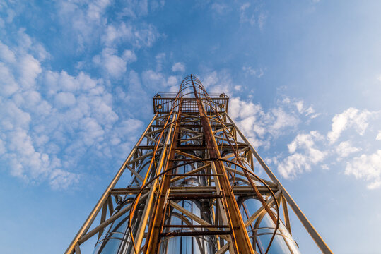 Bottom-Up View of Modern Industrial Steel Tower with Chrome Pipes | Golden Sunset Light on Metal Structure Against Blue Sky | Urban Architecture