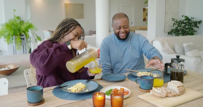 African couple at breakfast, woman picking glass, pouring juice from pitcher into glasses, toasting