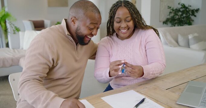 Couple signing contract at home, picking up blue key fob, pointing and celebrating new home