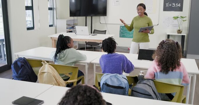 African American female teacher with tablet asking question engaging students to answer in class