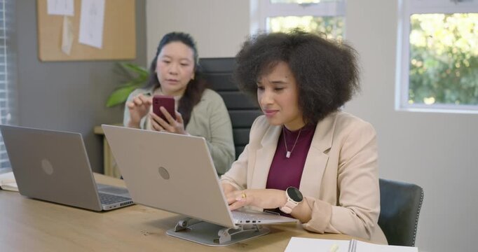 Diverse women in blazers at desk African-American reacting to laptop ping, typing while peer fixing