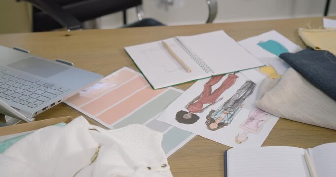 Camera is panning right to reveal layered fabric swatches and sketches on wooden table for design