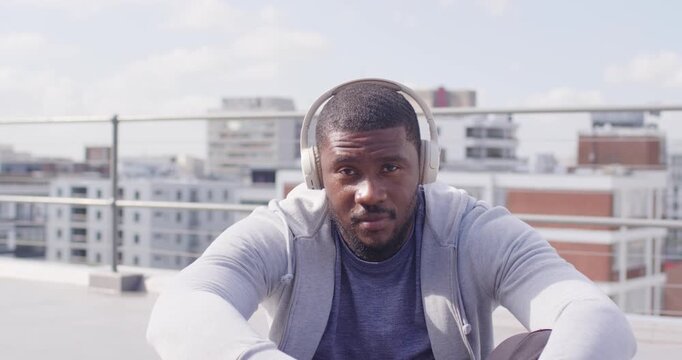 Mid adult African American man sitting rooftop hearing music on headphones, lifting head smiling