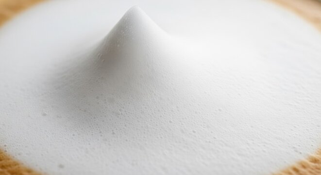 Detailed macro photography of a sharp stiff peak of white milk foam on a latte or cappuccino coffee surface, showing dense microbubbles and smooth velvety texture in high detail.