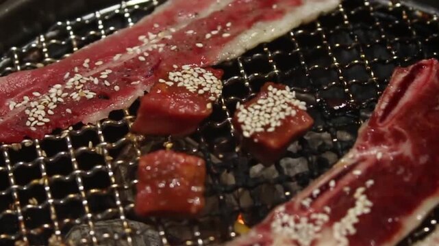 Close-up of premium marbled beef and seasoned meat sizzling on a Korean BBQ grill. Juicy cuts with sesame seeds over charcoal, perfect for food and restaurant footage.