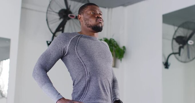 Mid adult man taking deep breath, hinging hips, folding to stretch in gym wearing athletic clothing