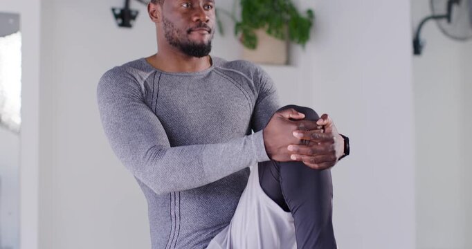 African male wearing compression top and watch raising knee to chest, balancing at gym warming up