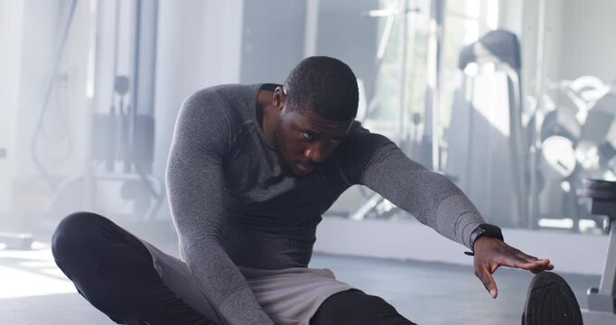 Man stretching leg on gym mat, reaching shoe, adjusting smartwatch, preparing workout