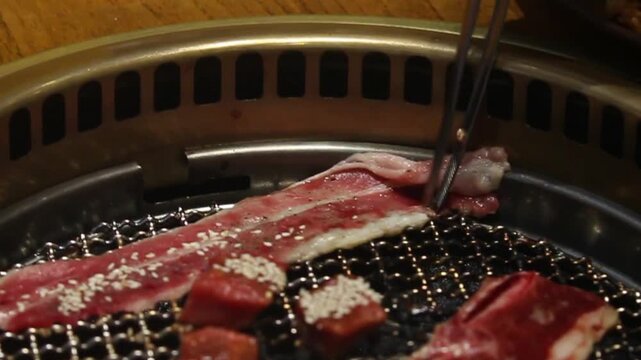 Close-up of premium marinated beef grilling on a Korean BBQ. Juicy meat sizzling over charcoal with sesame seasoning, perfect for restaurant, food, and cooking footage.