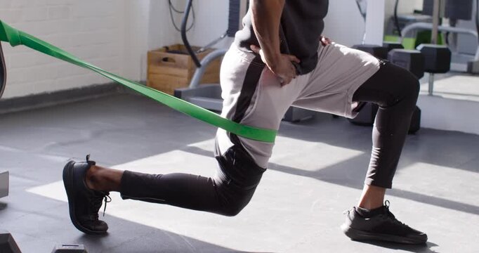 African American man performing lunges in gym studio with green band pulling hips back for strength