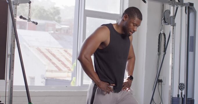 African American man doing lateral steps at gym, band pulling from rack, checking form, copy space