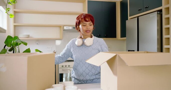 Adult African American woman unpacking boxes for kitchen setup, placing plant and stacking plates