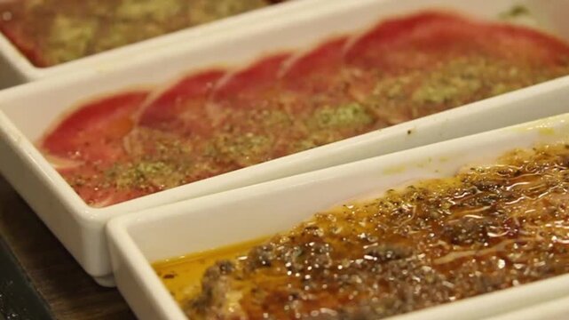 Close-up of thin raw beef slices marinated with herbs and seasoning in serving trays, prepared for grilling at an Asian barbecue restaurant.